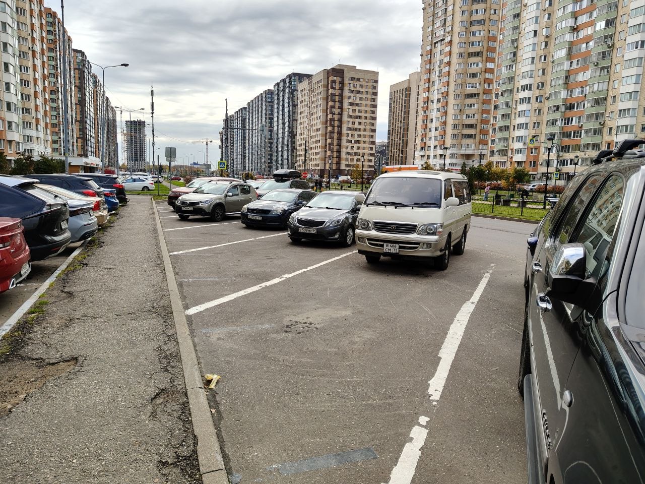 Широкий бульвар с парковкой вдоль домов, вдали новые корпуса и краны