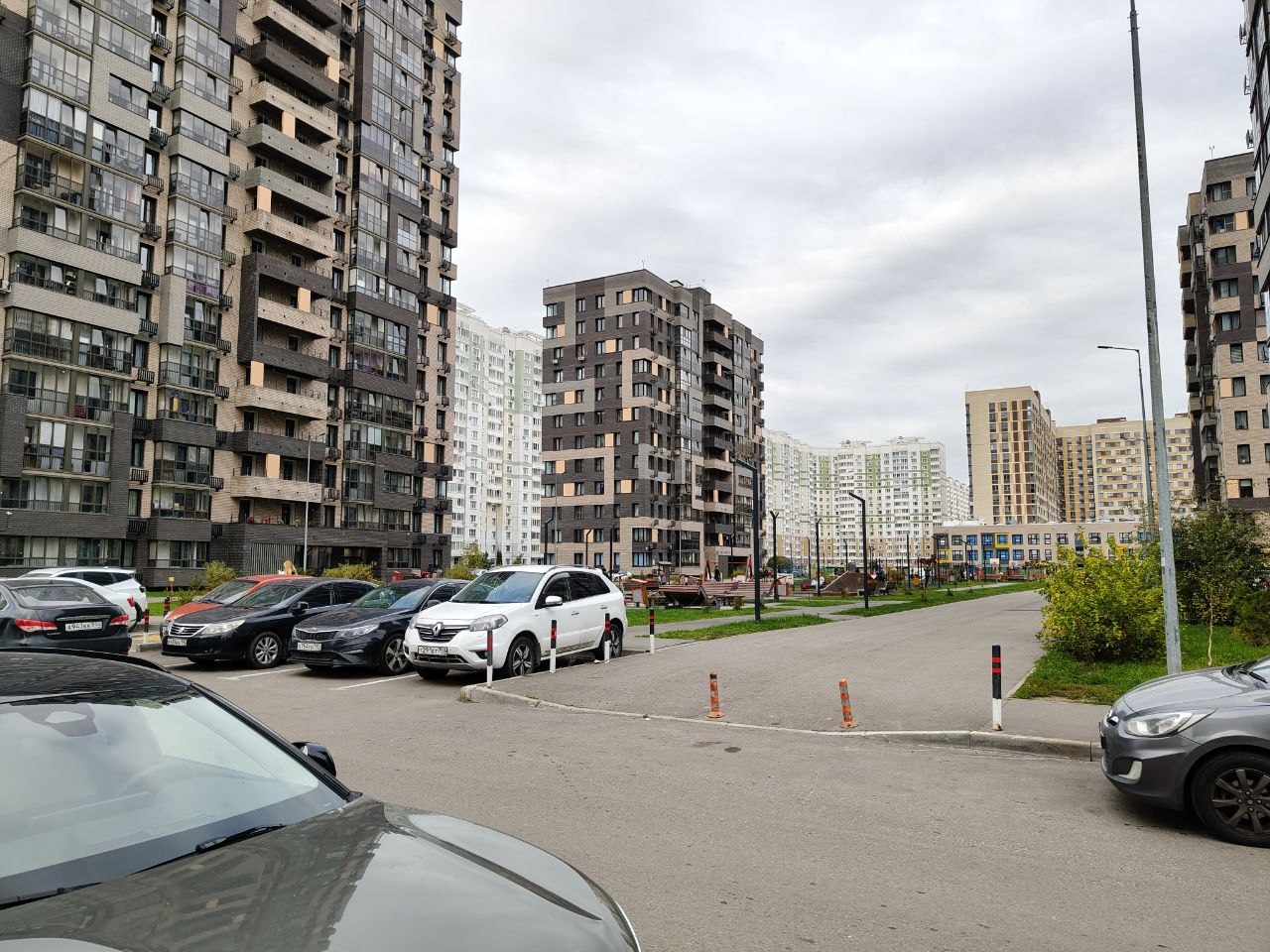 Въезд во двор: машины у края, дальше пешеходная зона с детскими площадками и цветным зданием школы